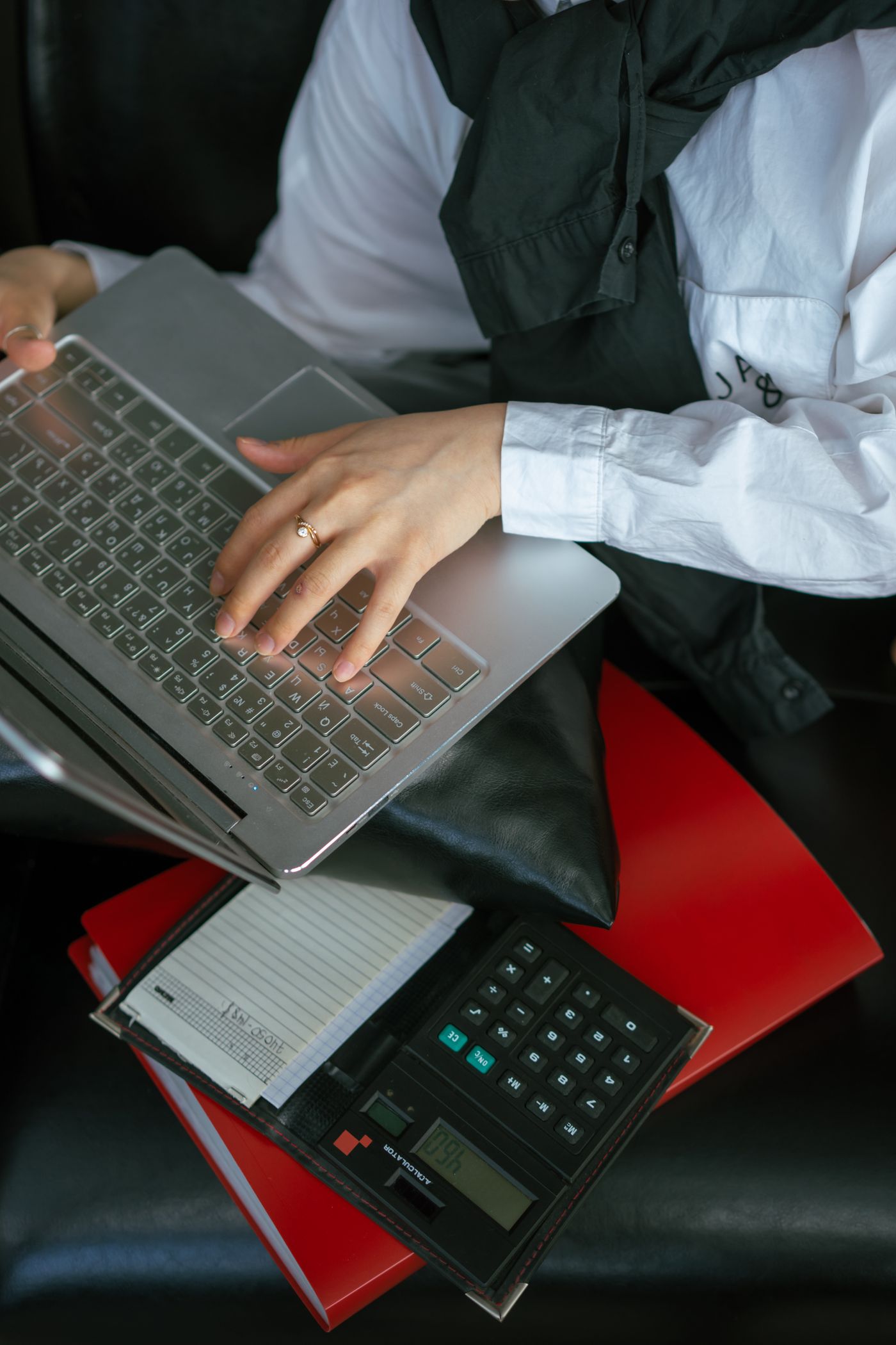 Hands working on a laptop beside calculation tools.